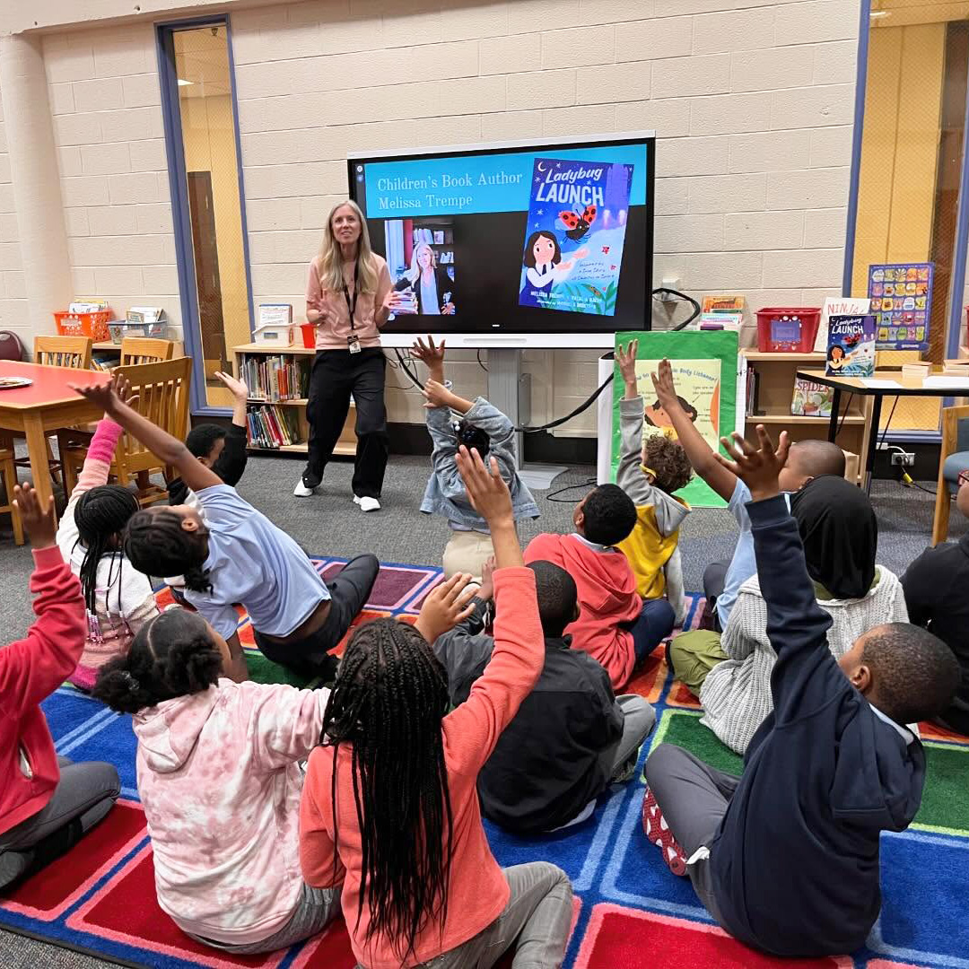 Students at Edward Heston School in Philadelphia raise their hands during an interactive author presentation and reading activity in the school library.