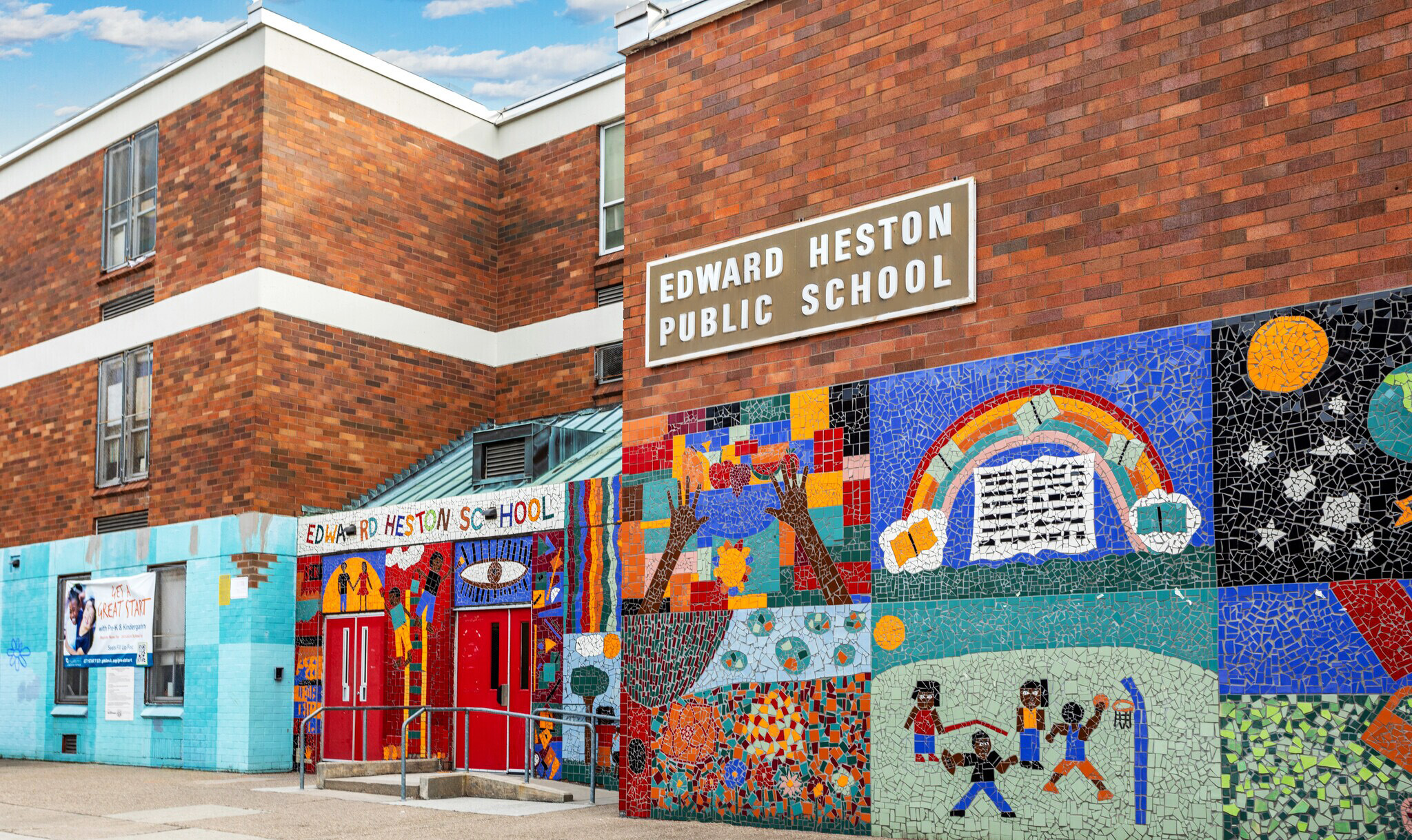 Exterior view of Edward Heston School in Philadelphia featuring colorful mosaic artwork, the main entrance, and the school name displayed on the brick building façade.